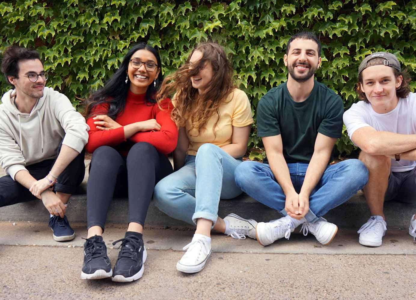 five young adults sitting on a kerb, smiling