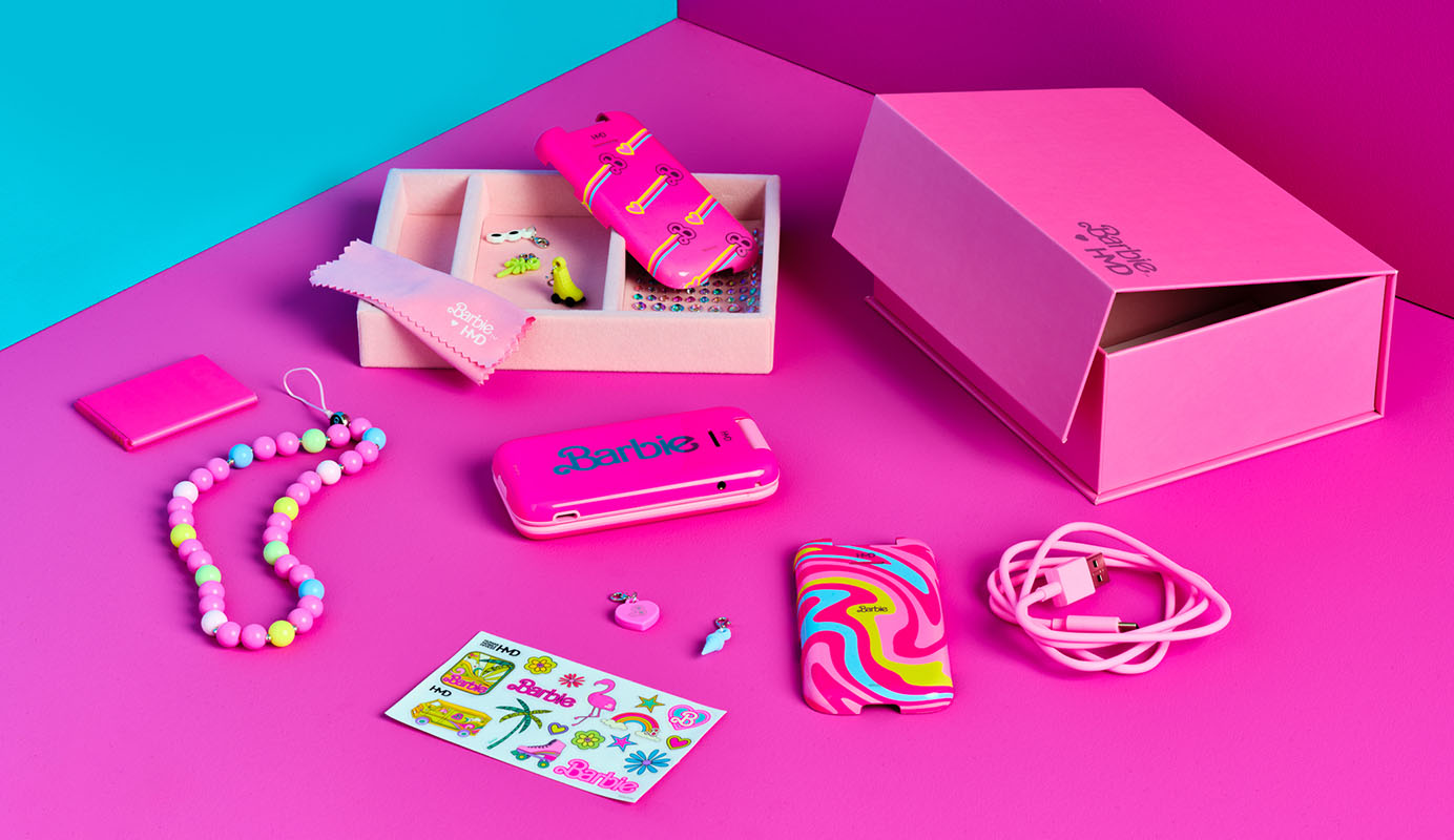 The HMD Barbie Phone, with its pink box and included accessories, namely charging cord, stickers, beaded lanyard, extra phone covers, attachable charms and gems.