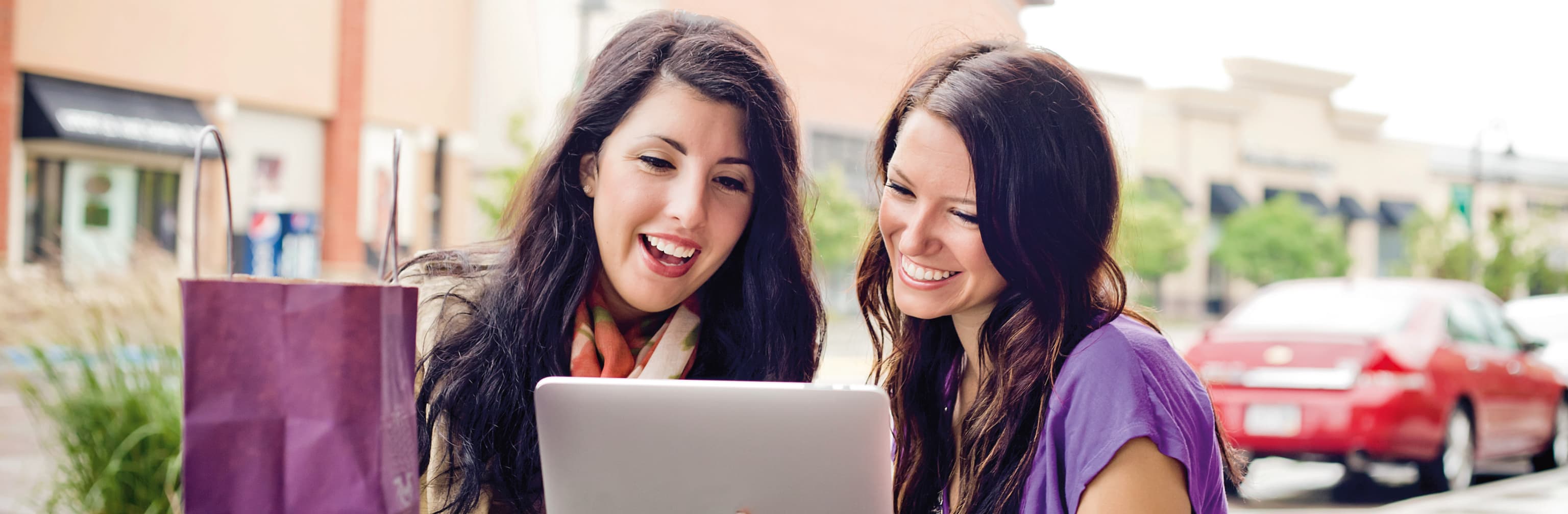 Two women smiling and looking at screen at cafe.